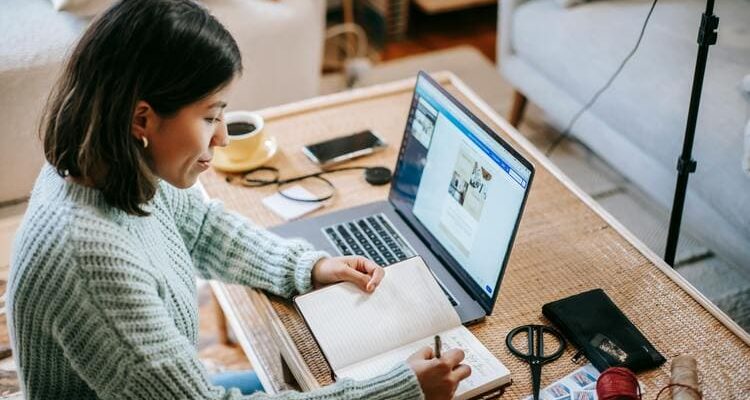 Young focused woman writing in planner while using laptop